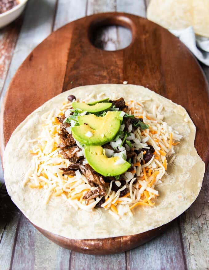 The birria meat and consommé is added, minced onions and cilantro and optional avocado too