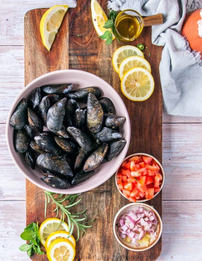ingredients to make mussel pasta including the mussels in a large colander, some fresh tomatoes, diced shallots, garlic, lots of lemon juice, butter and olive oil and herbs