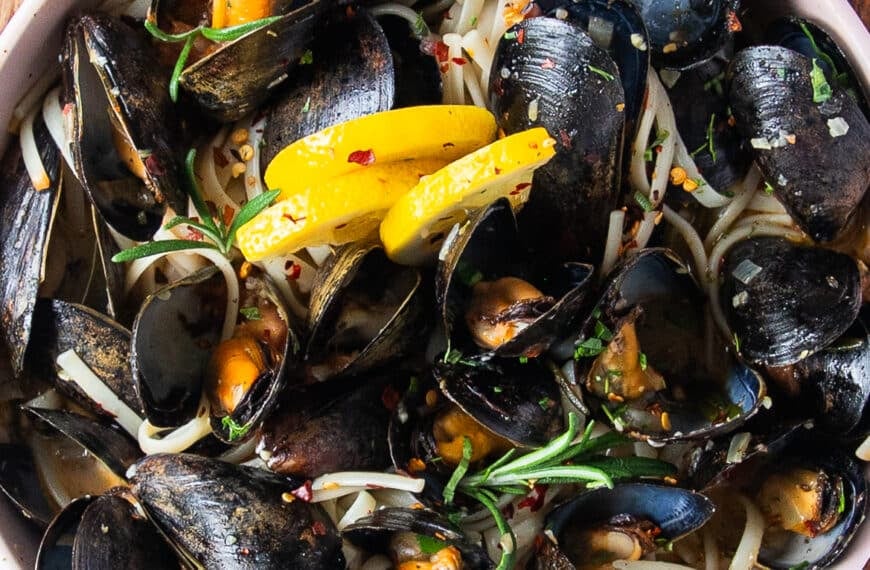 close up of a mussel pasta bowl with lemon slices and perfectly cooked mussels