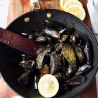 The mussels, seasoning and lemon slice is added to the skillet to make the sauce
