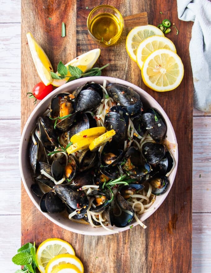 top view of a plate of mussel pasta with lemon wedges around and garnished with herbs and chili flakes