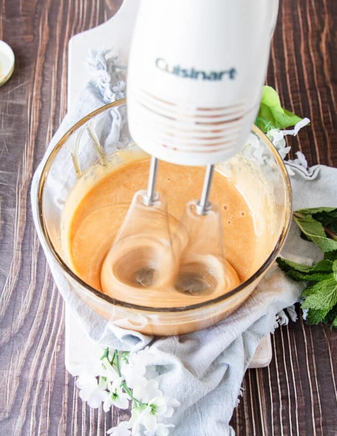 a hand held mixer whipping the honey in a glass bowl