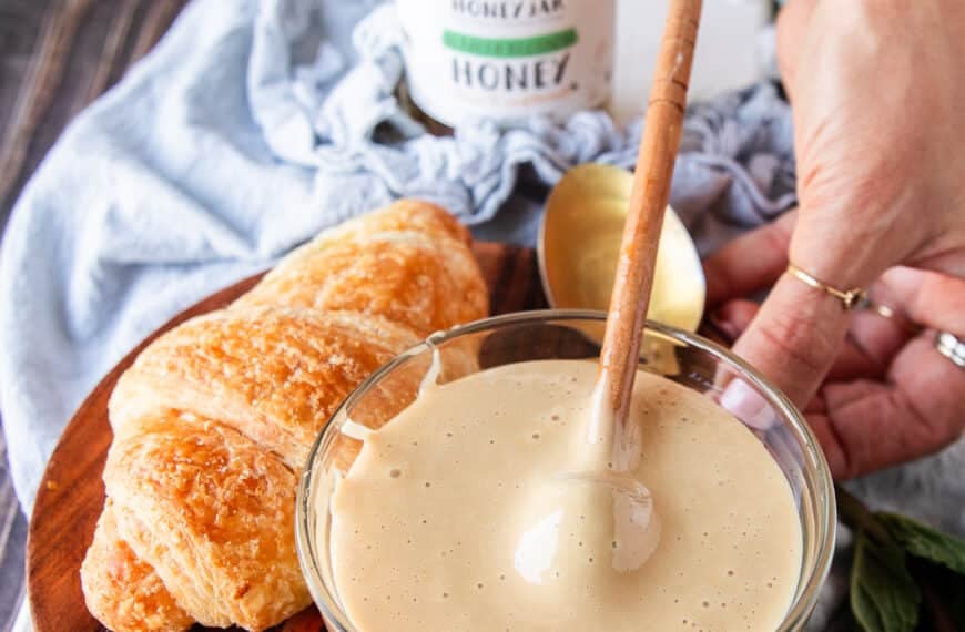 A bowl of whipped honey next to a croissant for spreading