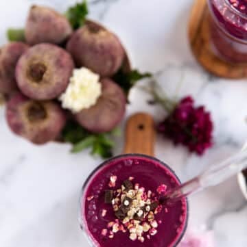 A beet smoothie with banana and honey in a cup with a glass straw