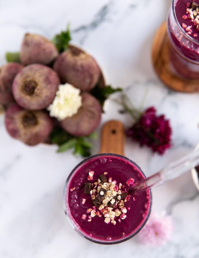 A beet smoothie with banana and honey in a cup with a glass straw