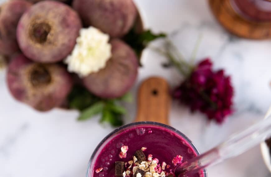 A beet smoothie with banana and honey in a cup with a glass straw